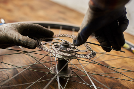 Cropped shot of mechanic making service in bicycle repair shop, repairing bike wheel using special tool, wearing protective glovesの写真素材