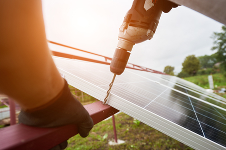 Close-up angled view of technician working with screwdriver connecting solar photo voltaic panel to exterior metal platform. Alternative renewable ecological green sun energy sources concept.の写真素材