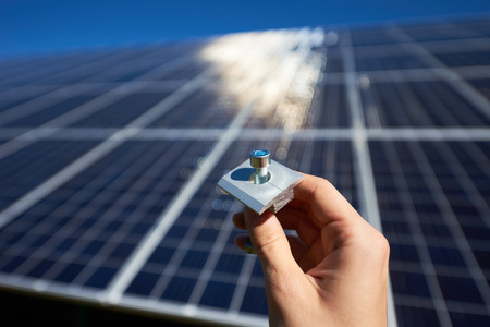 Mounters hand keeping little metallic screw twisted in the carving in front of big solar battery. Important details needing for innovative solar pannels mounting. Environment friendly, green energy.の写真素材
