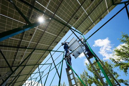 Three mounters holding solar panels on high metallic construction. Work, needing special equipment. Innovative exterior. Modern solution for natural resources saving, using renewable solar energy.の写真素材