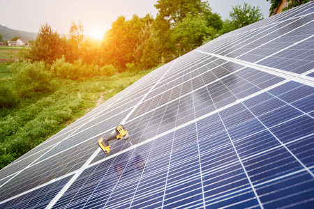 Close-up of screwdriver on shiny photo voltaic solar system surface on lit by sun green trees and grass background. Alternative energy, ecology protection and cheap electricity production concept.の写真素材