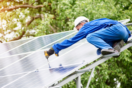 Team of two constructors connecting photo voltaic panel to stand-alone solar system platform using screwdriver. Alternative energy, professionally done job and profitable financial investment concept.の写真素材