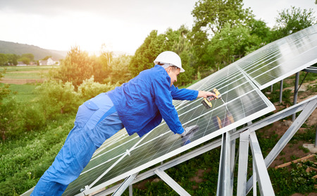 Construction worker connects photo voltaic panel to solar system using screwdriver. Professional installing and construction of solar system, alternative energy and financial investment concept.の写真素材