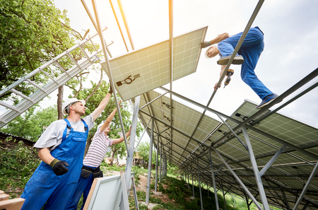 Stand-alone solar photo voltaic panel system installing. View from below of three technicians workers mounting heavy solar panel. Alternative energy production and professional construction concept.の写真素材