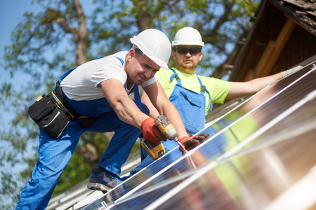 Two professional technicians installing solar photo voltaic panel to metal platform using screwdriver. Stand-alone solar system installation, alternative renewable energy generation concept.の写真素材
