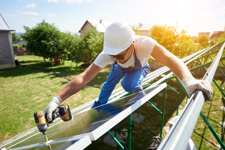 Using special drill, worker mounting solar panels on the roof. High-tech exterior, modern equipment, ecological frienly, green energy. Innovative electricity saving, using renewable energy of sun.の写真素材