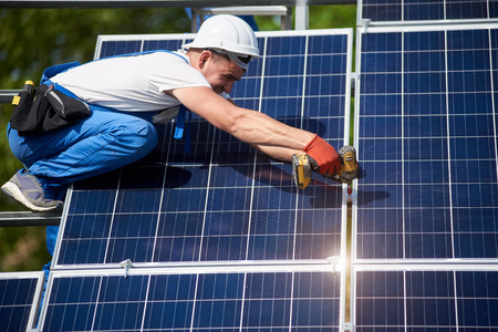 Professional technician installing solar panel to metal platform using screwdriver. Exterior solar system installation, renewable green energy generation concept.の写真素材