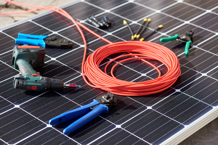 Close-up view of different details and instruments for mounting and connecting solar photovoltaic system. Objects laying on blue solar panel. Alternative energy resources renewable ecology concept.