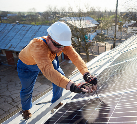 Male engineer installing stand-alone solar photovoltaic panel system. Electrician mounting blue solar module on roof of modern house. Alternative energy ecological concept.の写真素材