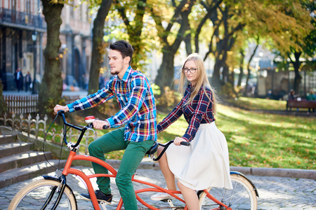 Young active happy traveler couple, handsome bearded man and pretty blond woman in glasses on tandem bike on bright sunny day on stony staircase and ancient building background.の写真素材
