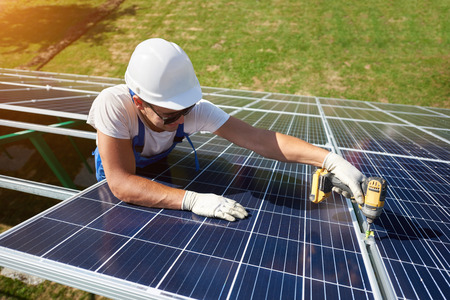 Professional worker installing solar panels on the green metal construction, using different equipment, wearing helmet. Innovative solution for energy solving. Use renewable resources. Green energy.の写真素材