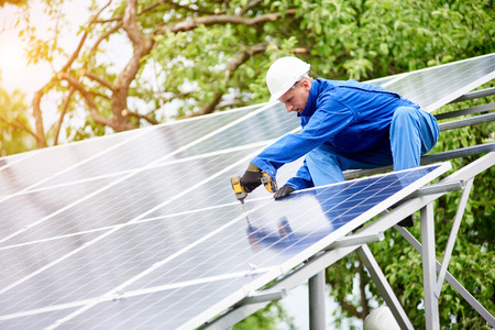 Young construction worker connects photo voltaic panel to solar system using screwdriver on bright sunny day. Alternative cheap sun energy production and profitable financial investment concept.の写真素材