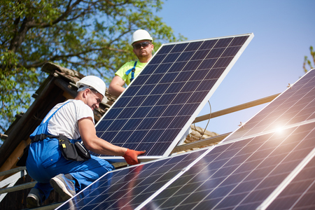 Two professional technicians adjusting heavy solar photo voltaic panels to high steel platform. Exterior solar system installation, alternative renewable green energy generation concept.の写真素材