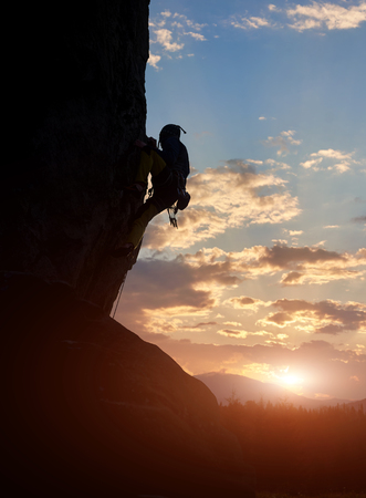 Side view of male silhouette climbing on natural rocky wall. Adrenaline, extreme, strength, ambition concept. Amazing mountain, sunrise with bright sunshine. Low angle view. Over filtered. Copy spaceの写真素材