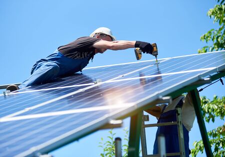 Professional workers team installing solar panels on the green metal construction using different equipment. Innovative solution for energy solving. Use renewable resources. Green energy.の写真素材