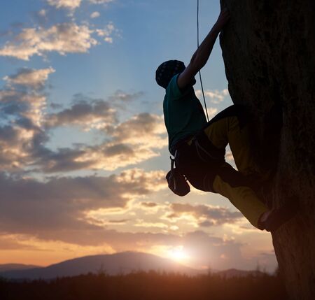 Silhouette of man climbing on rock. Climber training on natural relief. Extreme sport. Active recreation in nature. Overcoming difficult climbing route. Amazing sunrise sky over mountains in twilightの写真素材