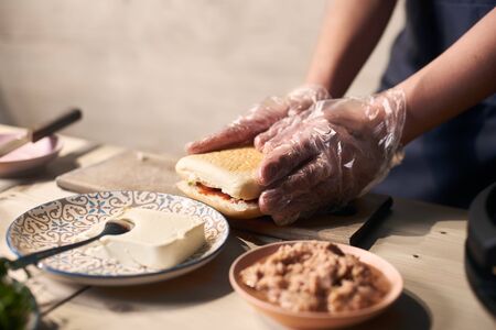 Detailed view of chef preparing gourmet burger with fish, cheese and vegetables. Process of cooking typical italian refreshments. Healthy alternative to grease. Selective focus. Blurred background.の写真素材