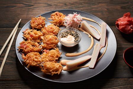 Close up view of delicious sushi with crab sticks on black plate served on the wooden table, decorated with chopsticks, bowl of soy sauce, and gingerの写真素材