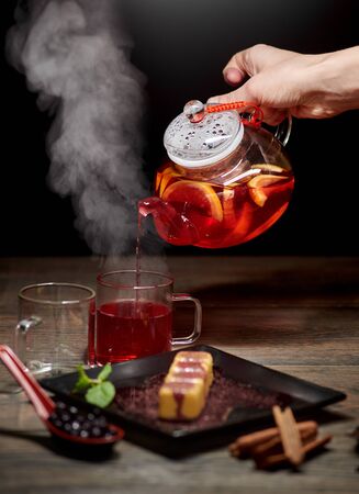 Delicious sweet sushi rolls served on black plate on the wooden table. Chef hand is pouring hot orange tea from the teapot into glass cupsの写真素材