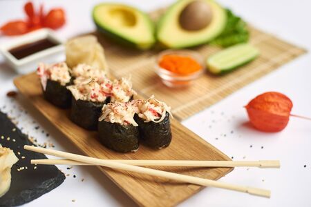 Crop of tasty sushi roll topped with chopped seafood sticks. Delicious Japanese dish served with wasabi, soy sauce and marinated ginger. Table decorated with physalis, caviar and different vegetables.の写真素材