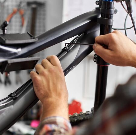 Cropped shot of male mechanic making service in bicycle repair shop, worker repairing bike using special instrumentの写真素材