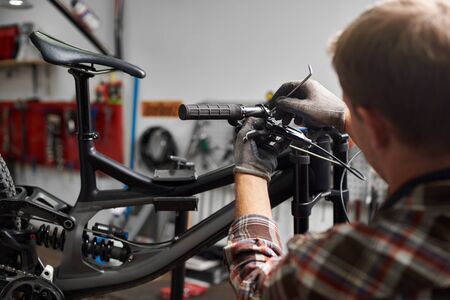 Cropped shot of male mechanic making service in bicycle repair shop, fixing bikes parts using special tool, wearing protective glovesの写真素材