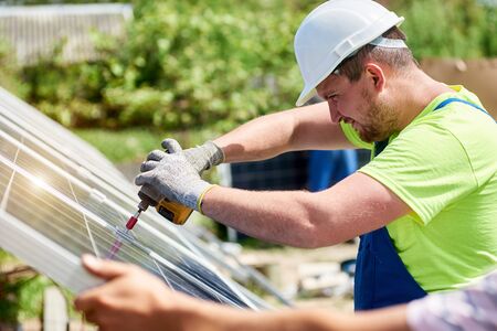 Professional technicians connecting exterior solar photo voltaic panel to metal platform using electrical screwdriver on green leaves summer bokeh background. Stand-alone solar system installation.の写真素材