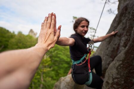 Young female rock climber hanging on safety harness and rope. Man helping his friend and climbing...