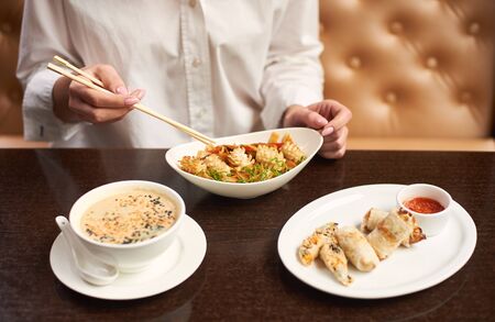 Woman in white blouse sitting in luxury restaurant and eating tasty meal. Three courses lunch from soup, noodles and tempura shrimps on special offer. Girl with manicure tasting oriental style dish.の写真素材
