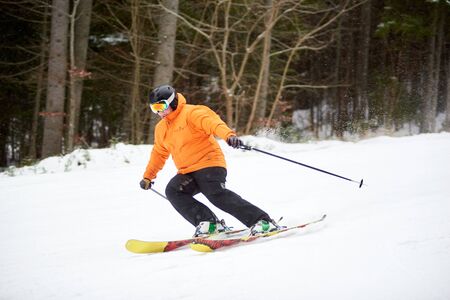 Adult man skiing and bending on side for doing turning. Dark view of forest along the mountain slope on background. Concept of healthy lifestyle and active winter outdoors pastime in wild nature areaの写真素材