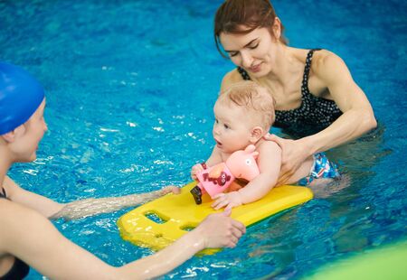 Swimming instructor teaching and helping little baby floating in blue water using auxiliary swimming tools for protection. Family healthy active lifestyle, early development, happy childhood conceptの写真素材