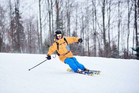 Front view of young man skier making turn on other side for next arc of skiing on snow-covered way. Professional skiing technique. Monochrome winter nature view. Bare trees on blurred background.の写真素材