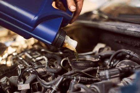 Engine oil changing and maintenance gear car engine in auto service workshop. Process of pouring motor oil into engine from blue bottle in dirty cropped hand. Close up side cropped snapshotの写真素材