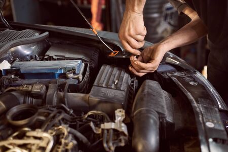 Cropped hands of unrecognizable mechanic doing car service and maintenance. Close up. Repairman with screwdriver working for fixing parts under hood machine. Blurred backgroundの写真素材