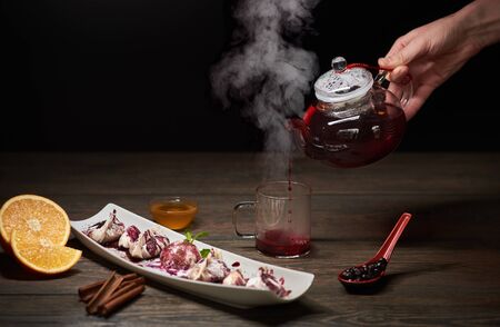 Delicious sweet sushi rolls served on white plate on the wooden table. Chef hand is pouring hot orange tea from the teapot into glass cupの写真素材