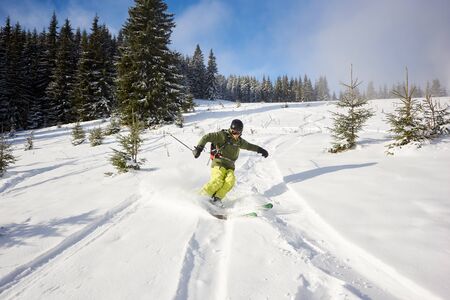 Male person skiing on wide open ski runs in downhill. Skiing down between fir trees. Spending time traveling and skiing. High mountains and nature in bright sunny day on background. Front view.の写真素材