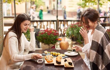 Best friends meeting in oriental restaurant and enjoying dinner. Colleagues eating delicious sushi coming with wasabi and ginger on lunch. Sisters talking and relaxing on balcony with tasty food.の写真素材