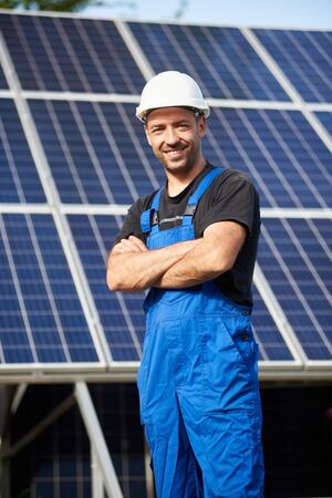Portrait of smiling successful male engineer technician standing in front of unfinished high exterior solar panel photo voltaic system blue shiny surface.の写真素材