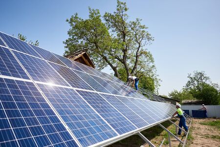 Two technicians installing solar panel photo voltaic system installation on steel platform on bright sunny summer day under blue sky. Renewable ecological green energy production concept.の写真素材