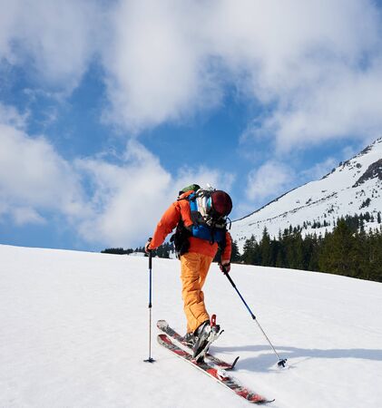Back view of ski mountaineer walking up along snowy ridge with the skis in the backpack. In background a blue sky. Snow and winter activities, skitouring in mountains.の写真素材