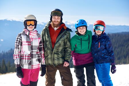 Group of happy people, man, woman and two kids smiling in camera on background of winter woody mountains, white snow and bright blue sky. Sport, recreation and friendship, family hobbies concept.の写真素材