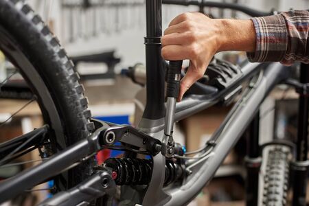 Cropped shot of man mechanic working in bicycle repair shop, worker repairing mountain bike using...