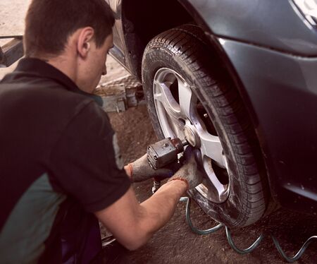 Changing car wheel in auto repair service. Focus on professional mechanic hands with pneumatic wrench, changing tyre of car. Cropped back view of worker on foreground. Maintenance and people conceptの写真素材
