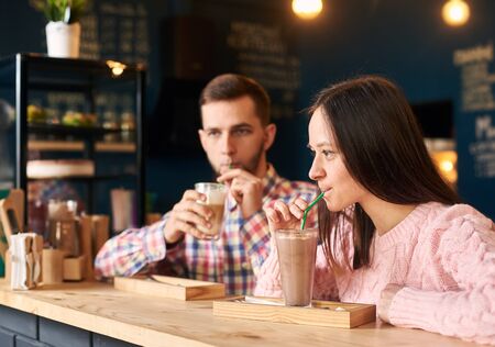 Young stylish happy couple sitting at cafe table, drinking coffee. Young man and woman at coffee...