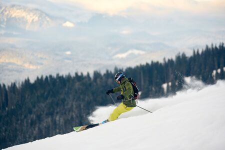 Skier descending at high speed from snow-covered mountain peak. Proficient skier with backpack. Extreme back-country skiing concept. Amazing nature mountains view from high ski slope. Side view.の写真素材