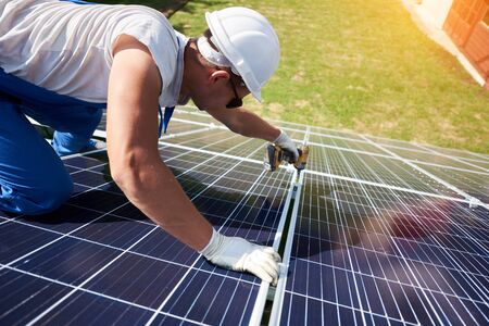 Professional worker installing solar panels on the green metal construction, using different equipment, wearing helmet. Innovative solution for energy solving. Use renewable resources. Green energy.の写真素材