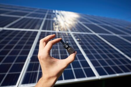 Mans hand keeping tiny detail for solar battery installing in front of solar pannel on background. Sunblinds on smooth surface. Innovative high-tech exterior. Environment friendly.の写真素材