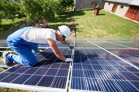 Professional worker installing solar panels on the green metal construction, using different equipment, wearing helmet. Innovative solution for energy solving. Use renewable resources. Green energy.の写真素材