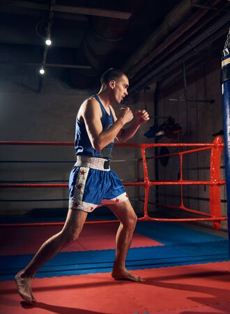 muscular sportsman kick boxer training hard boxing and preparing for fight, kicking and punching heavy boxing bag near the ring at the sport clubの写真素材