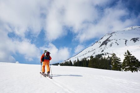 Back view of skier tourist backpacker hiking on skis up hill on background of blue sky and beautiful mountain. Winter vacations, active lifestyle, skiing and recreation concept.の写真素材